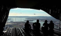 A photo of four Airmen watching C-17 flying from the open door of another C-17.