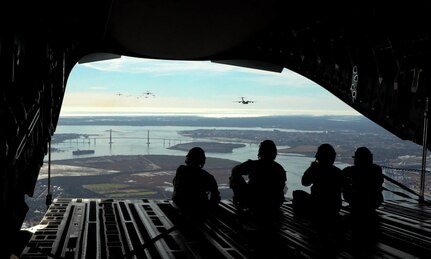 A photo of four Airmen watching C-17 flying from the open door of another C-17.