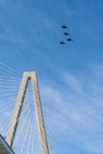 A photo of four F-16s flying over a bridge.