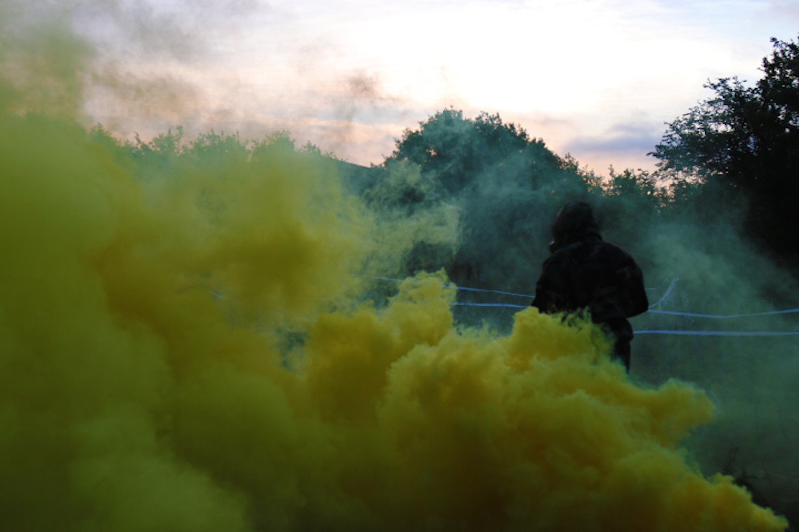 A soldier wearing a hazmat suit walks in back of a thick cloud of smoke.