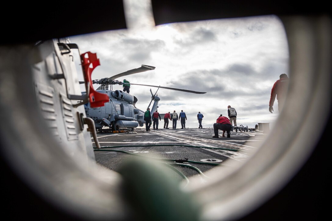 Sailors check for debris on the flight deck of a ship.