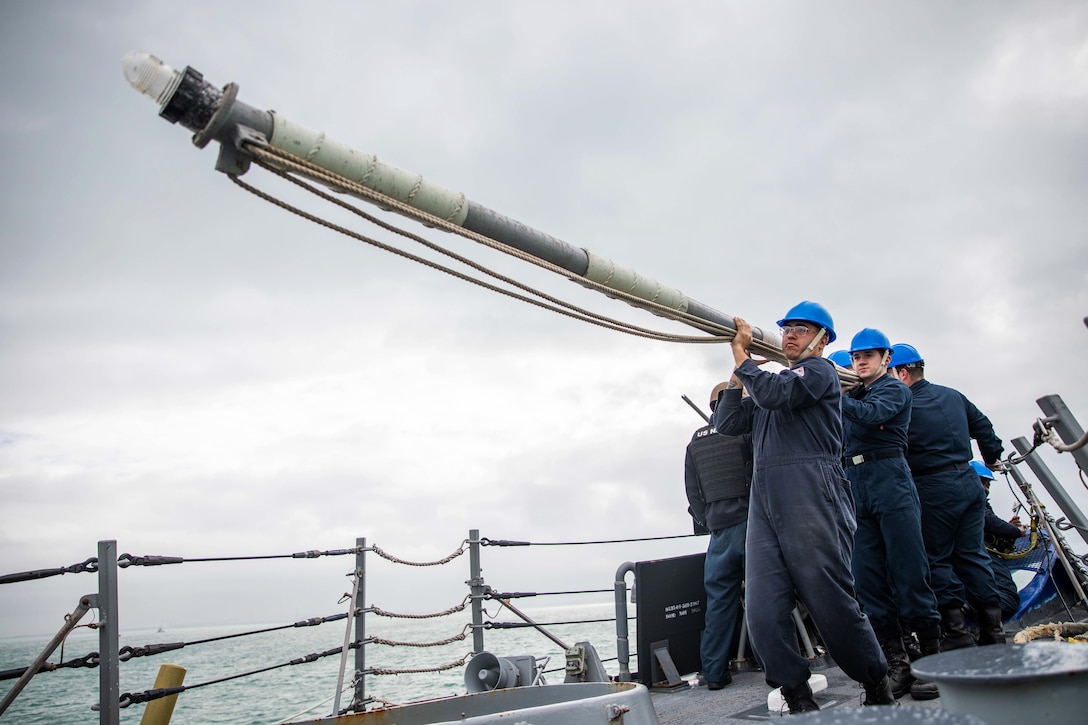 Sailors remove a flagpole on a ship.