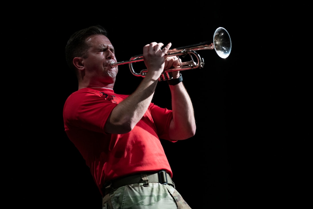 A soldier blows hard on a trumpet during a performance.