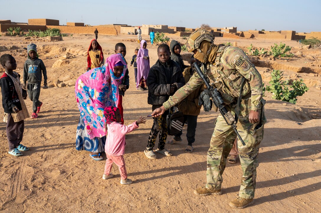 An airman gives a piece of candy to a young child.