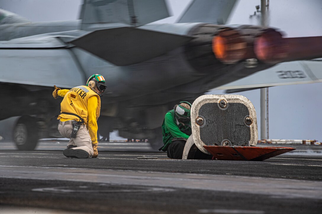 A sailor gives the go-ahead for a large fighter jet to launch from a ship.