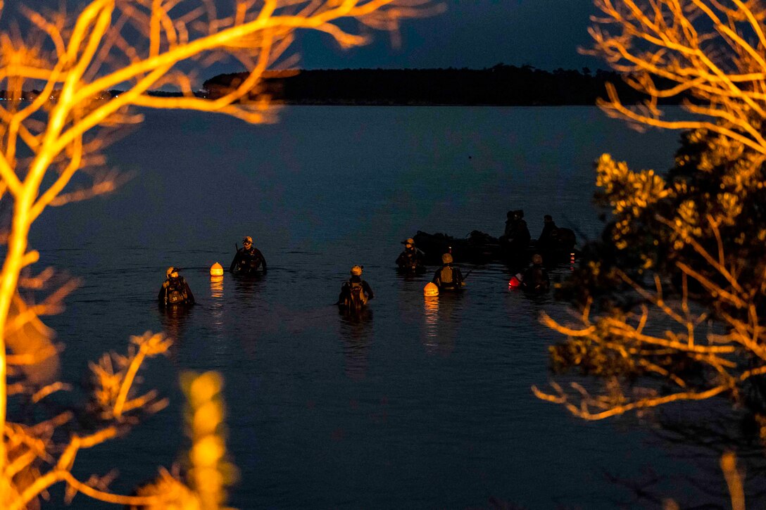 Marines wearing dive gear swim in water at night.