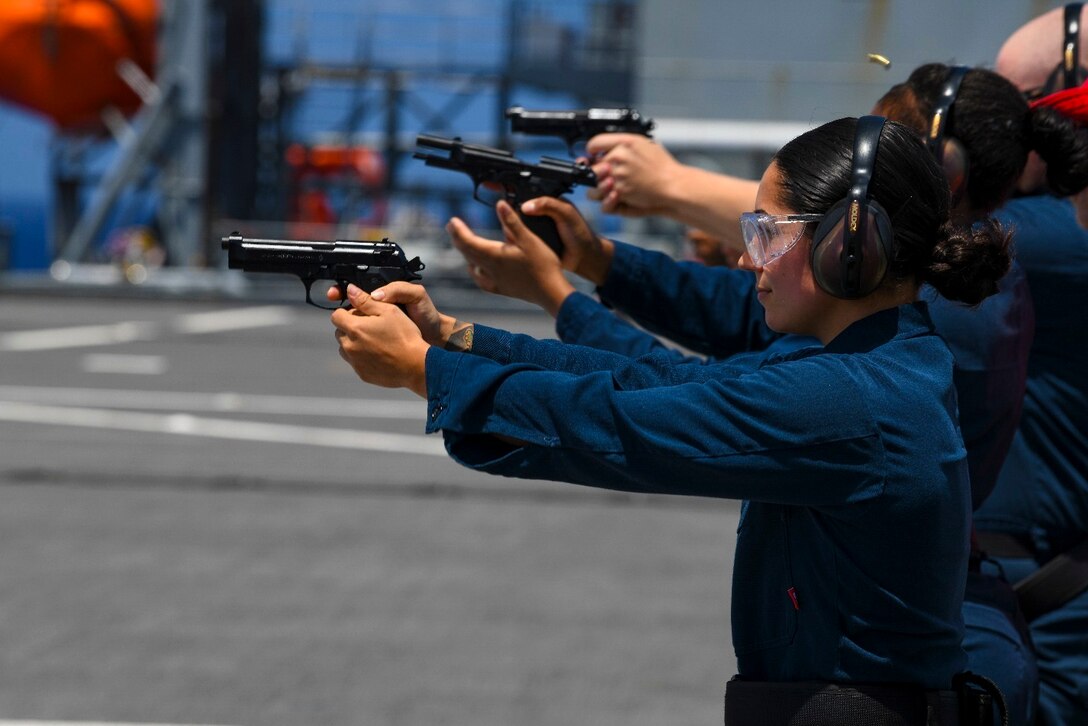 Sailors fire pistols at a target.