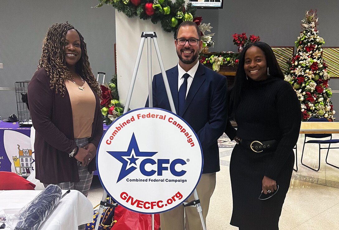 Two black women and a white man stand behind a round sign that says CFC.