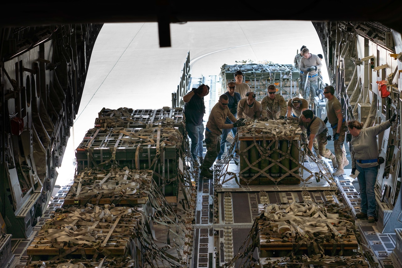 Airmen maneuver pallets of cargo into the hold of an aircraft.