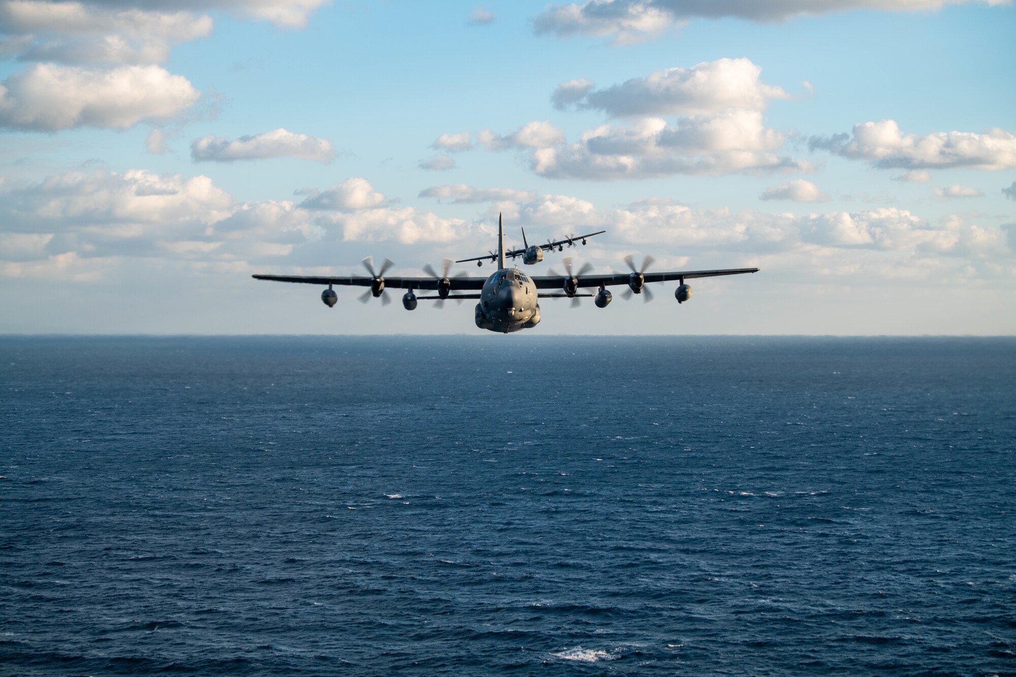 Two aircraft fly in formation over the ocean.