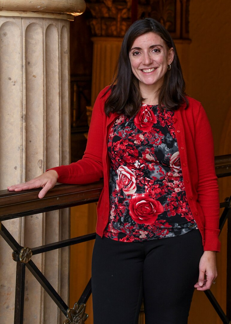 Female in red shirt stands with arm on ledge next to a marble column
