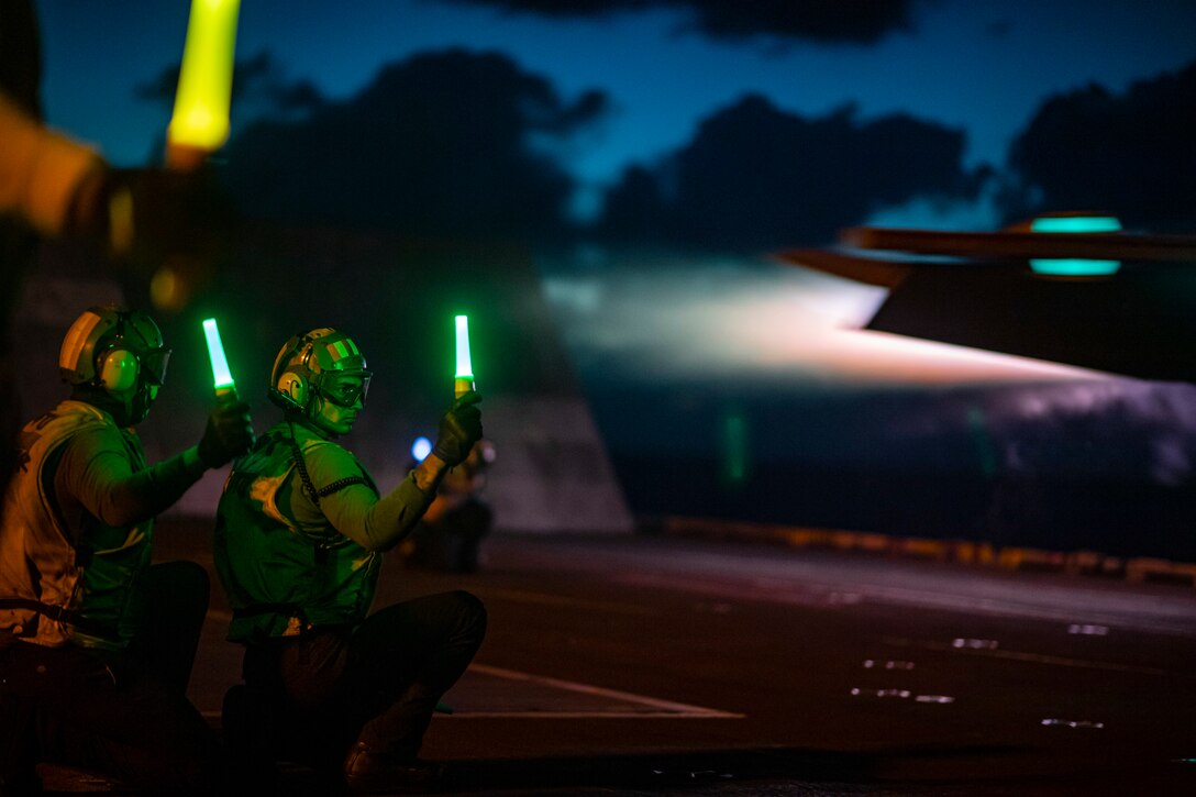 Sailors use lights to guide the launch of a jet from an aircraft carrier at night.