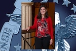 Female in red shirt stands with arm on ledge next to a marble column