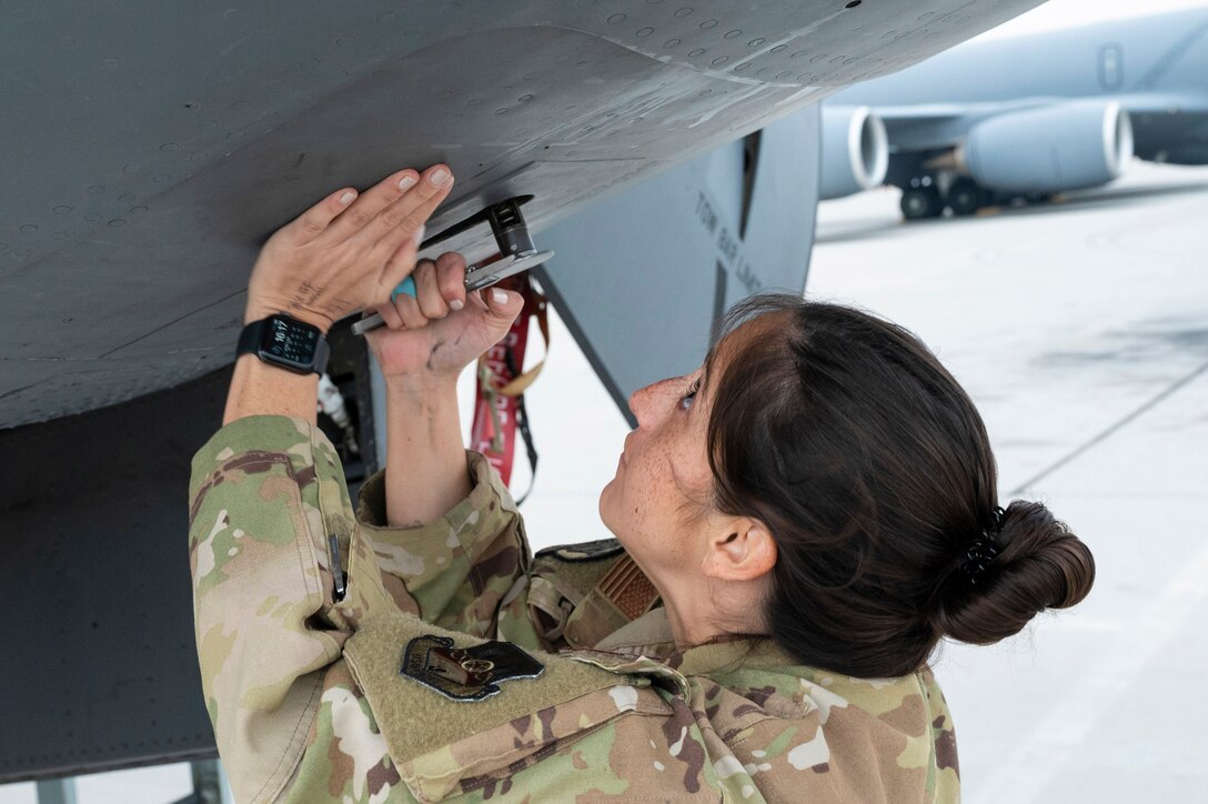 An airman works on the underside of an aircraft on a flight line.