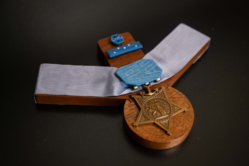 A medal attached to a ribbon sits on a wooden pedestal.