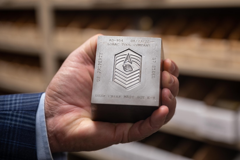 A hand holds a steel die with a mold cut into it.