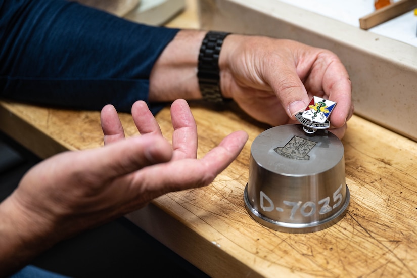 A hand holds a metal pin beside a matching steel mold.