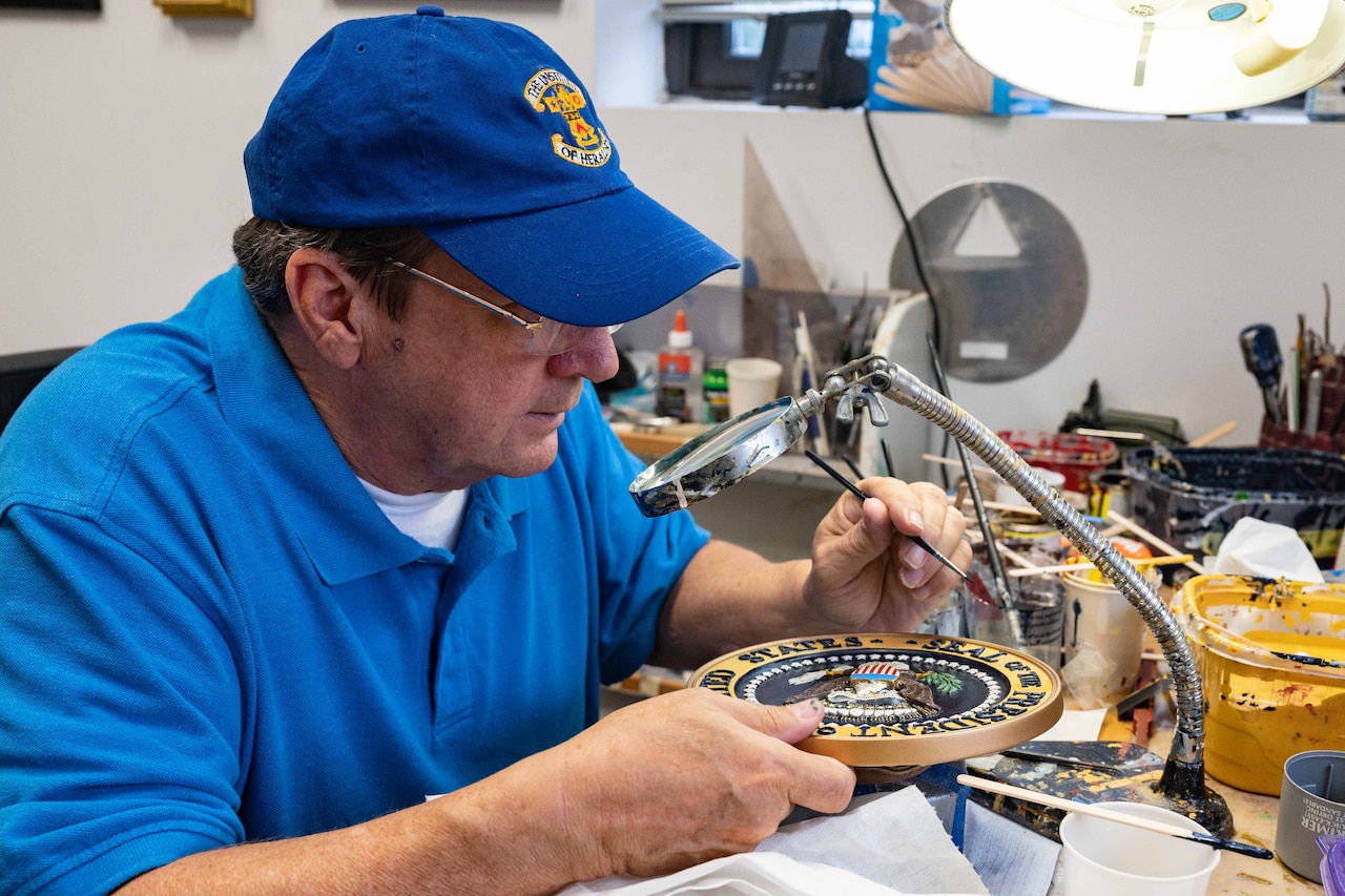 A man uses a magnifying glass to paint a seal.