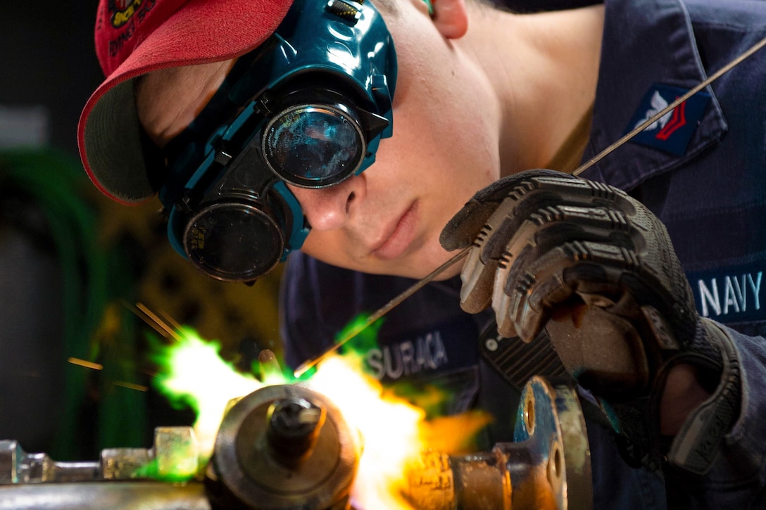 A sailor wearing protective gear burns a small pipe.