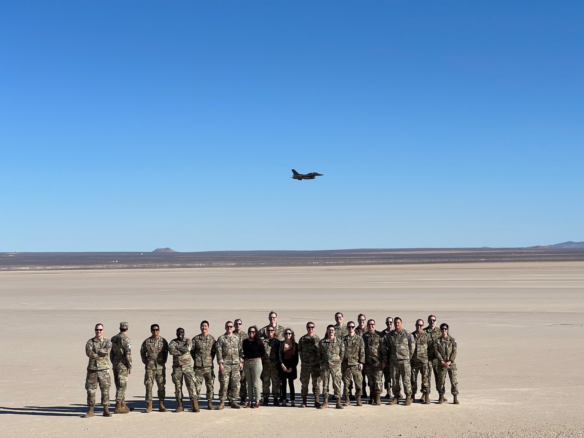 Savannah Langer, center, Arnold Engineering Development Complex aerospace engineer and her Space Test Course classmates stand as a group while an F-16 flies overhead.