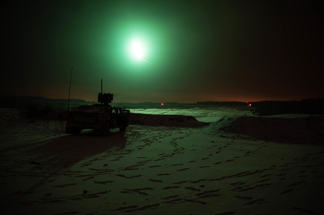 A military vehicle is parked in a flat training area at night, with green light illuminating the scene.