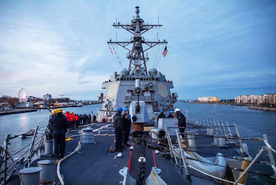 Sailors work on the deck of a ship that is approaching a port.