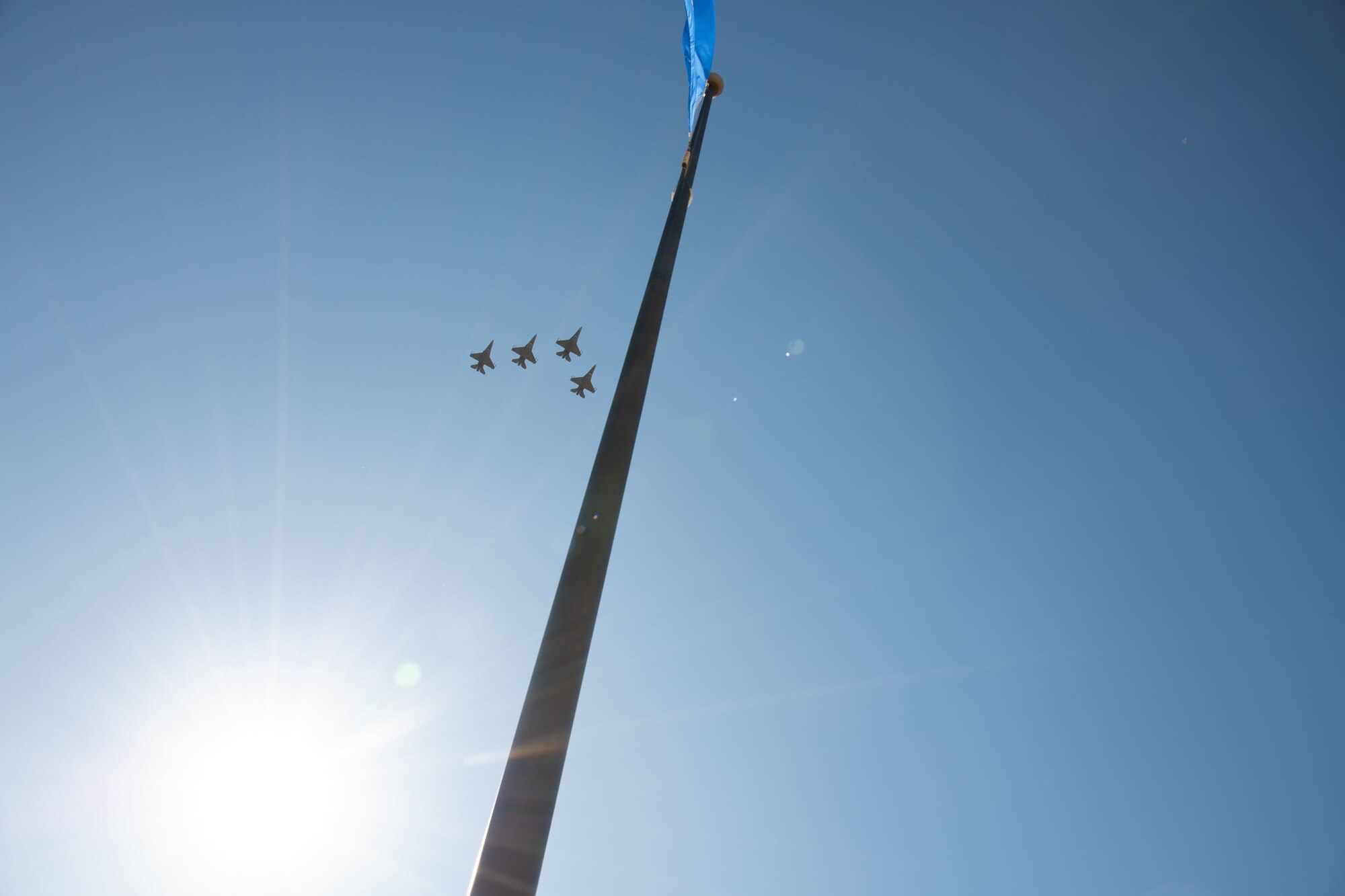 four f-16s fly across the sky near a flagpole flying the Oklahoma State Flag