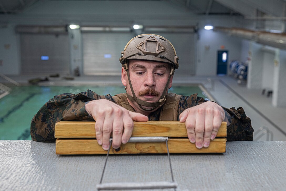 A uniformed Marine emerges from a swimming pool using a ladder.