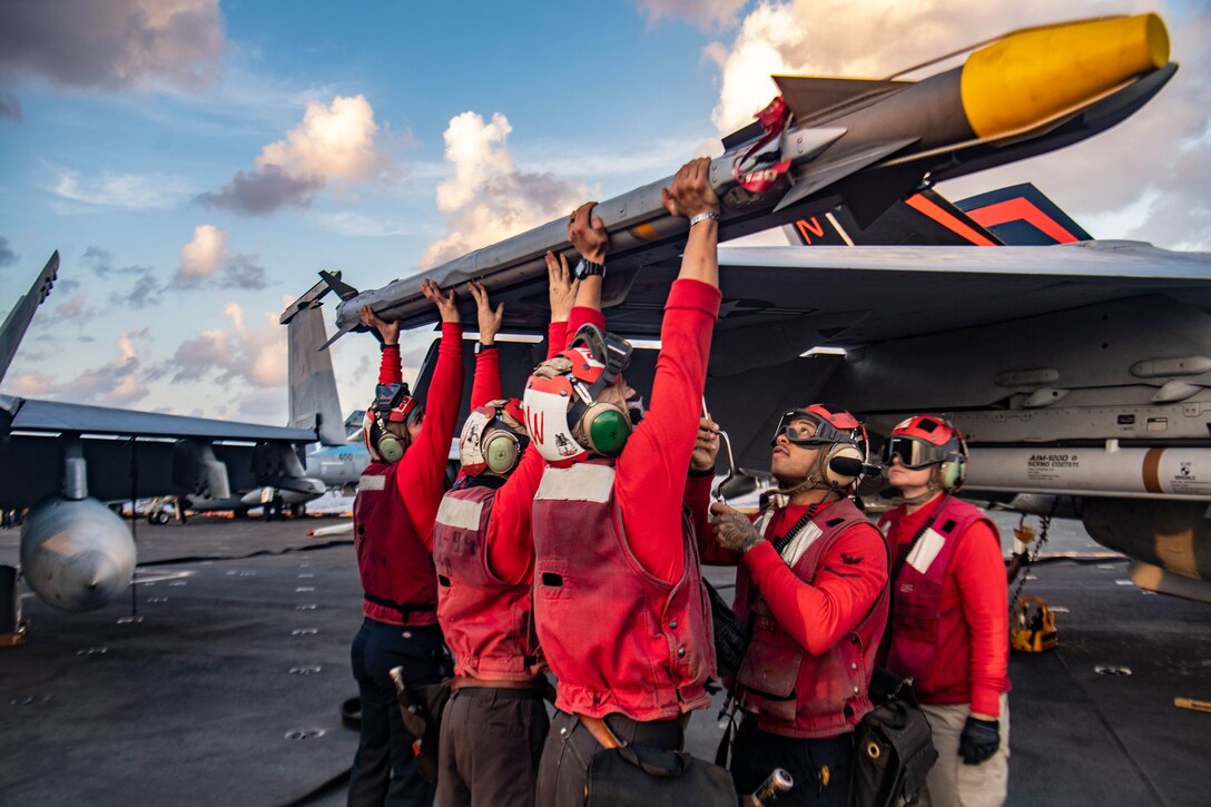 Sailors lift a missile above their heads while standing on a Navy ship.