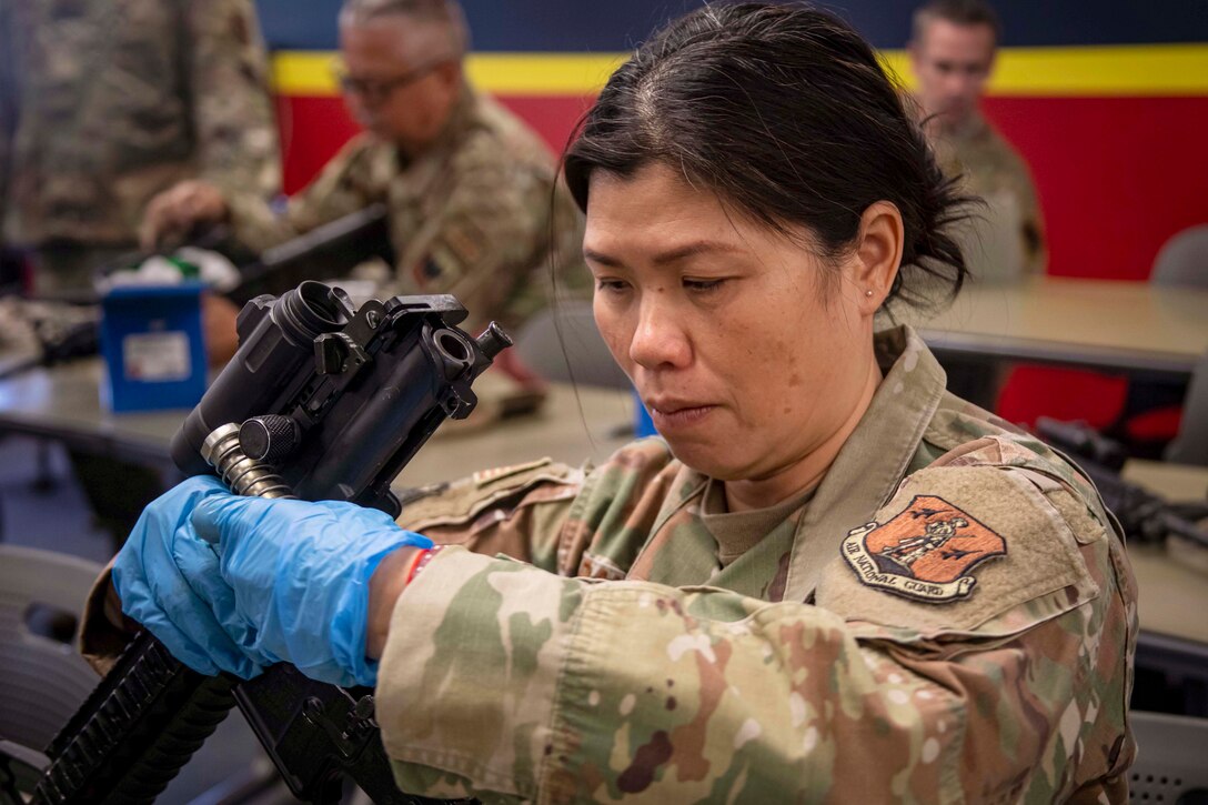An airman wearing protective gloves takes apart a weapon.