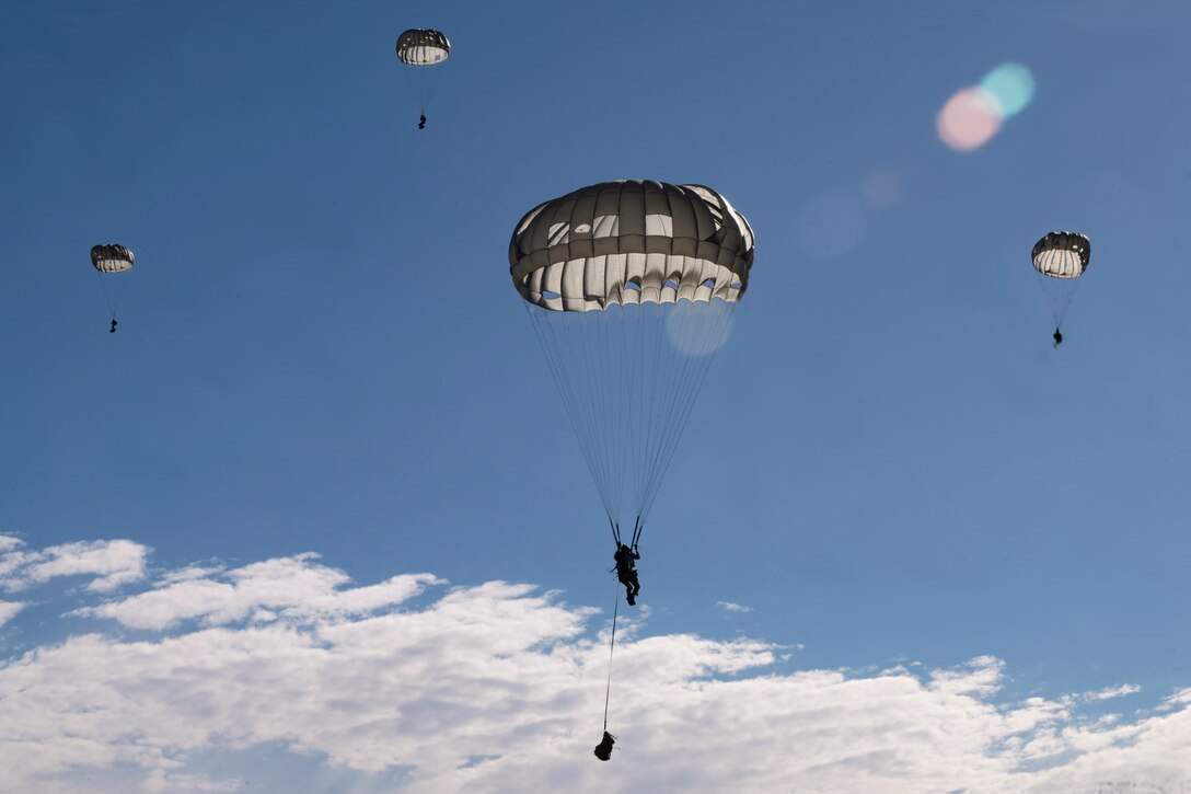 Four airmen free fall with parachutes.