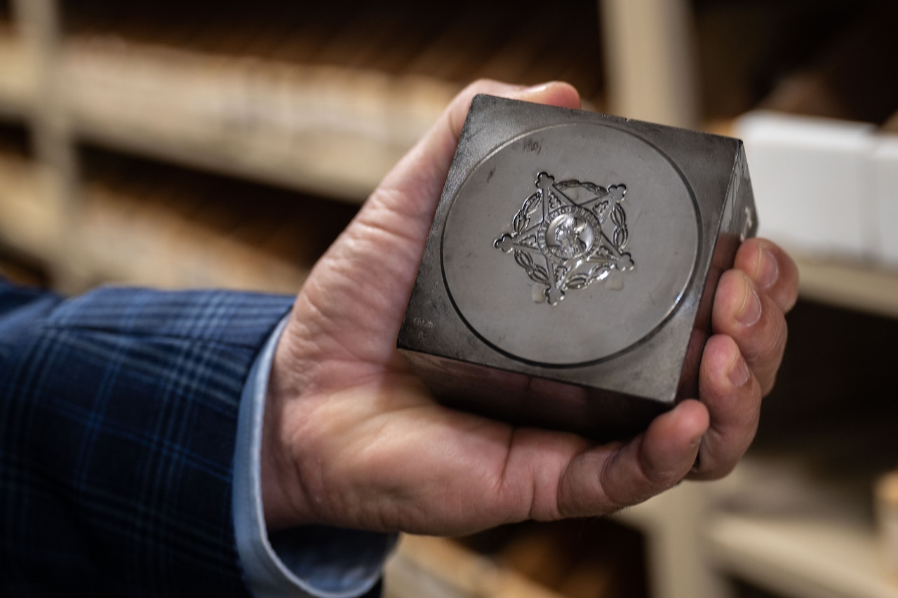 A man holds a steel die that shows the stamp of the Medal of Honor cut into it.