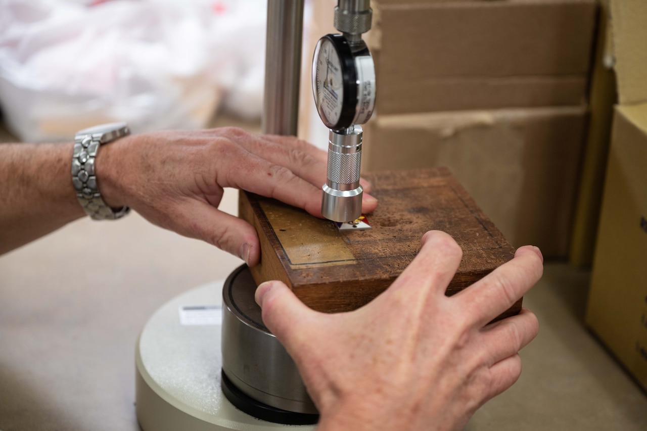 A small machine touches a metal pin attached to a piece of wood.