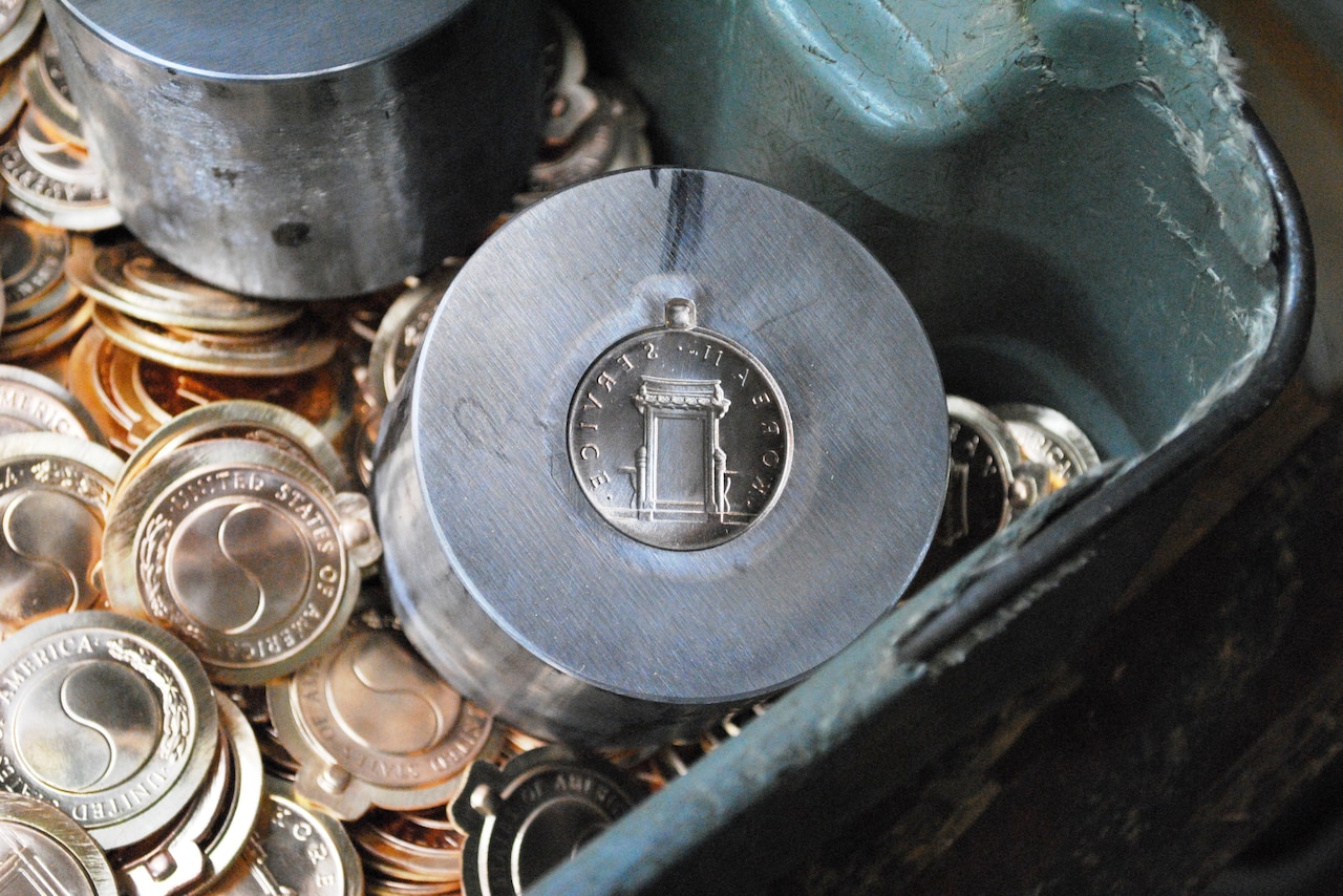 Two steel dies sit in a bucket of small metals produced from the dies.