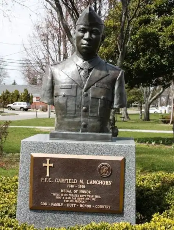 A bust of a soldier stands in a hedge of a small park.