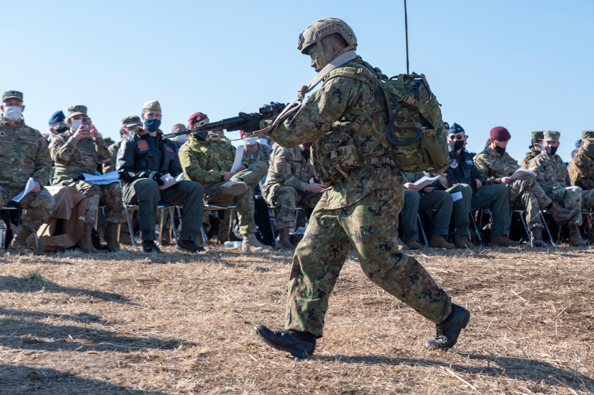 A well equipped Japanese soldier jogs past a large crowd of military officers