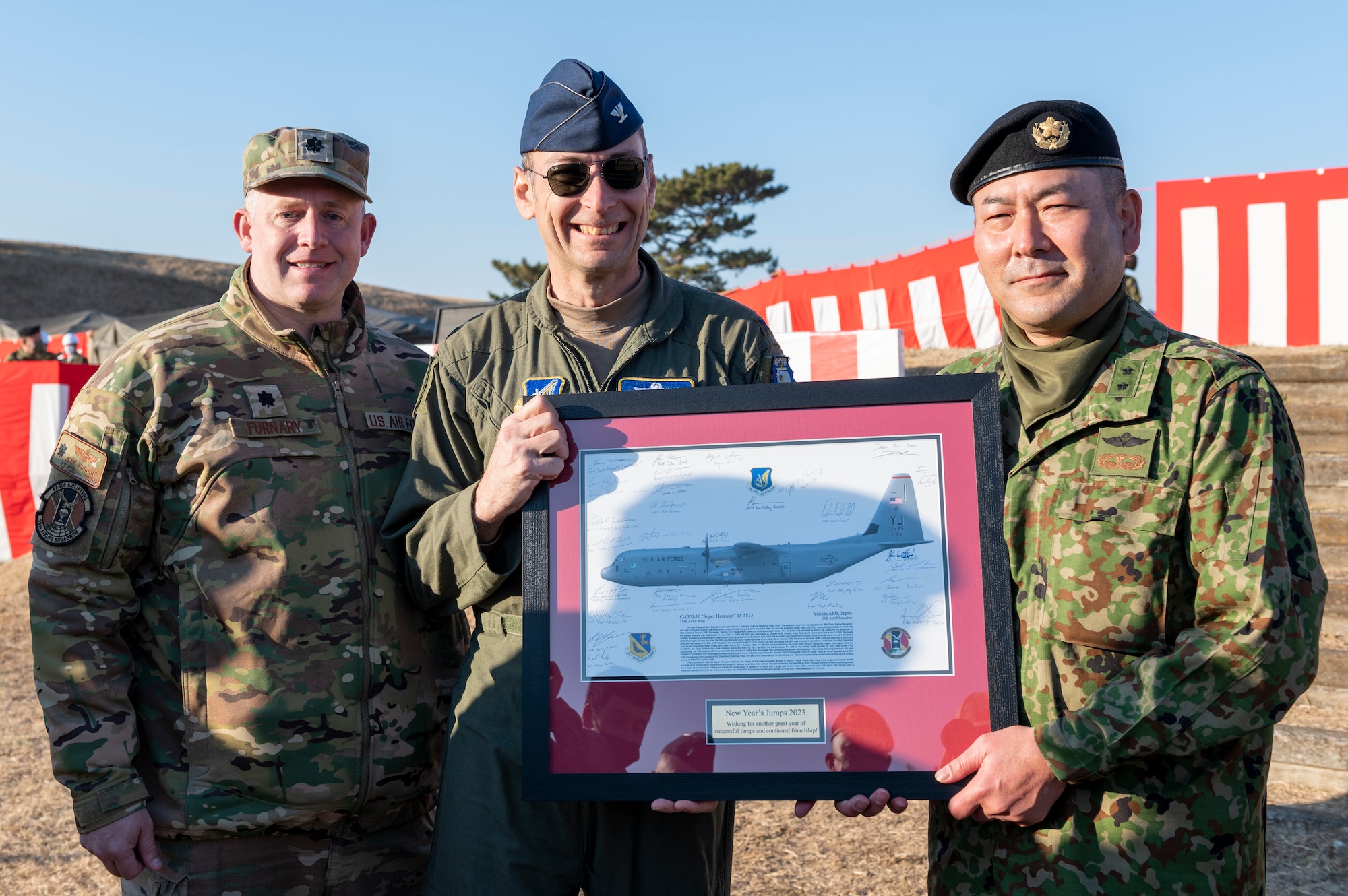 Three soldiers pose for a photo while holding a framed picture