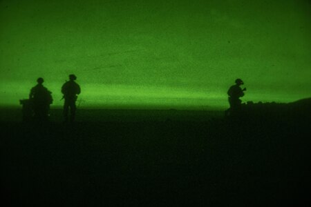 Soldiers walk across open terrain as seen through night vision lens.