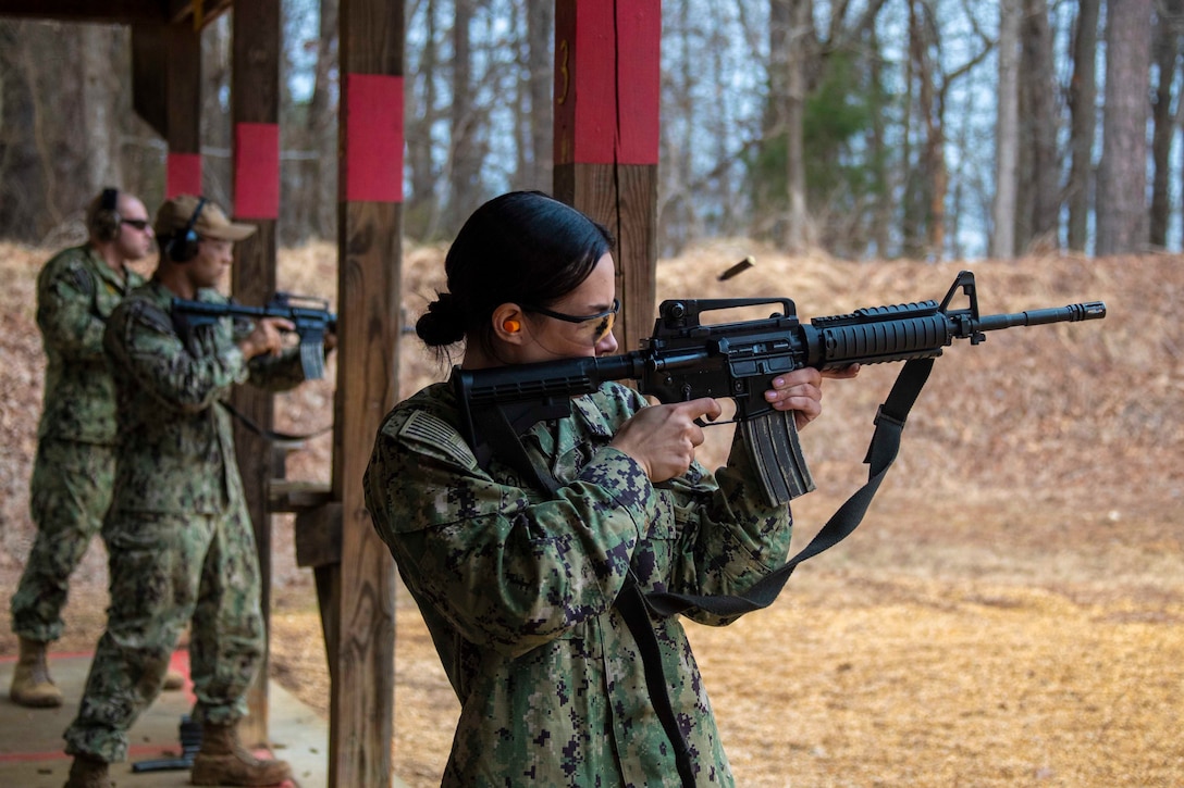 An airman fires a weapon as two others stand behind her.