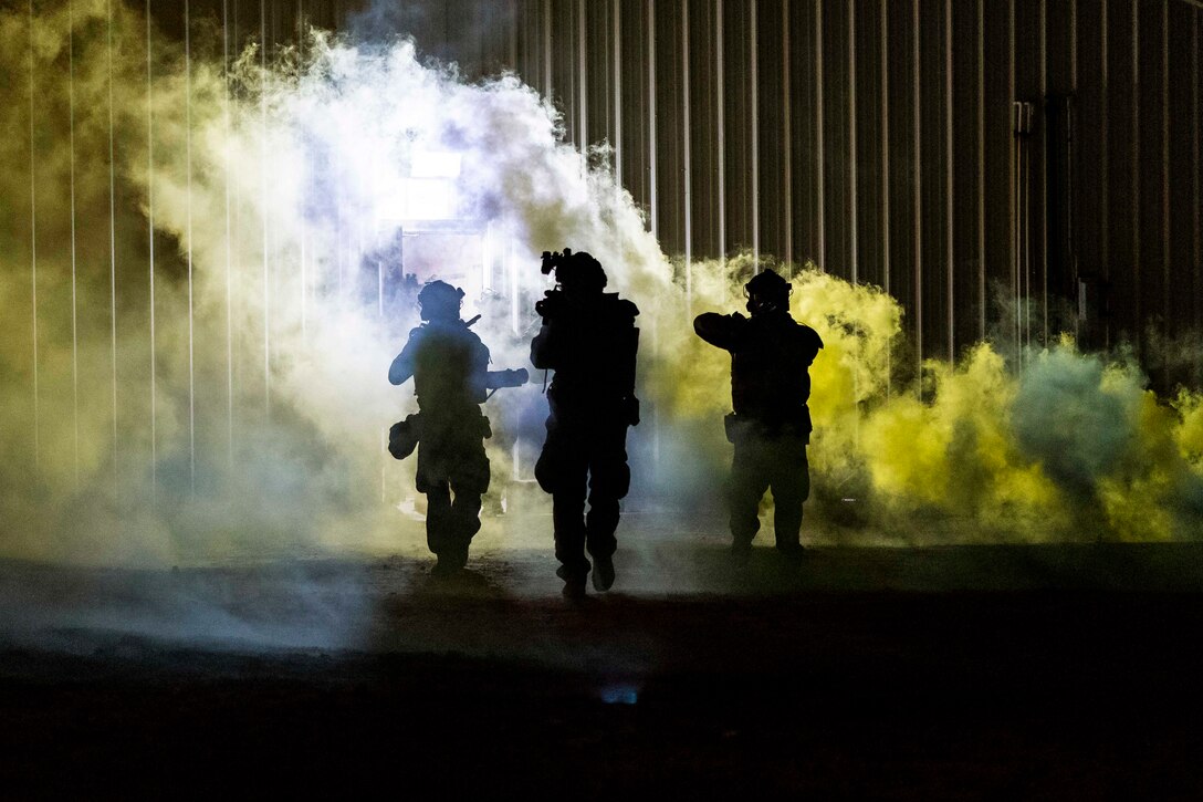 Three Marines shown in silhouette move through a smoke-filled building.