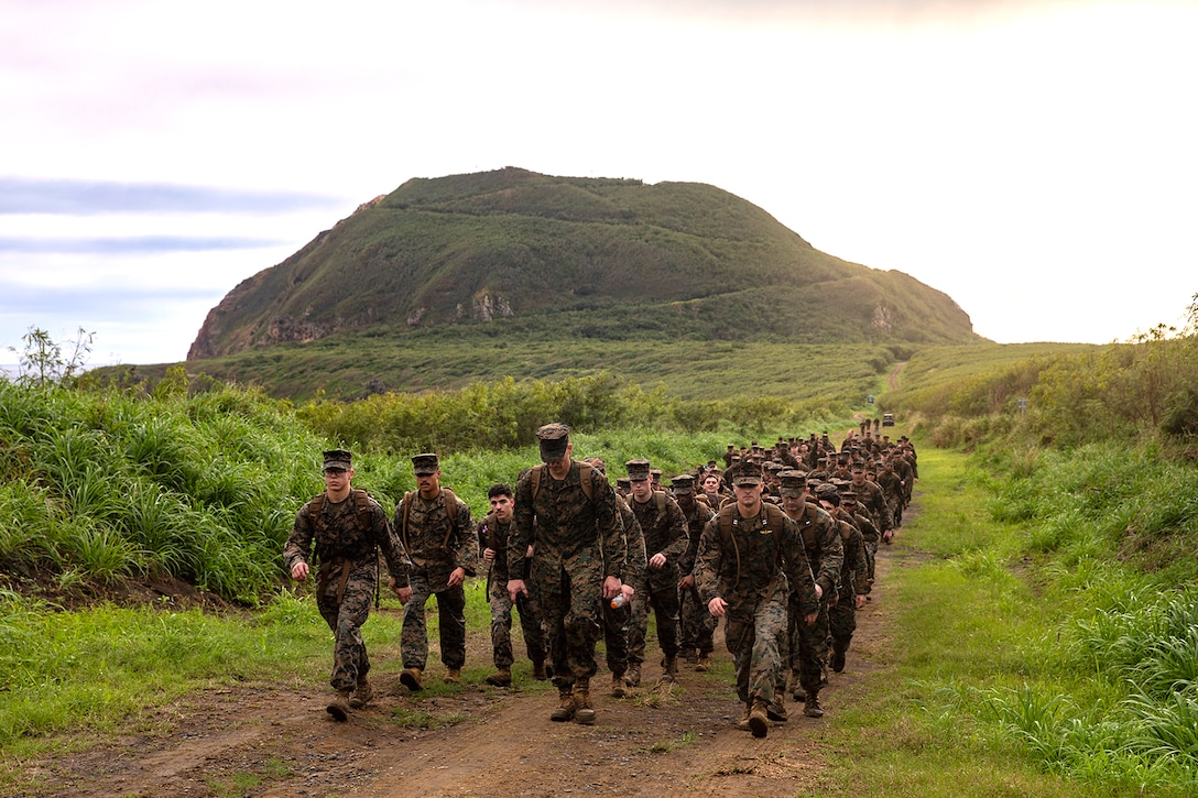 A group of Marines and sailors hike in a mountainous area.