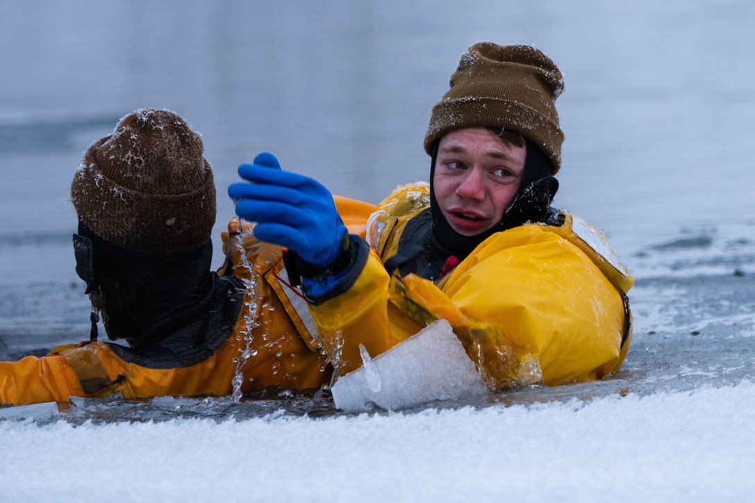 Two service members are shown close up while floating in icy water.