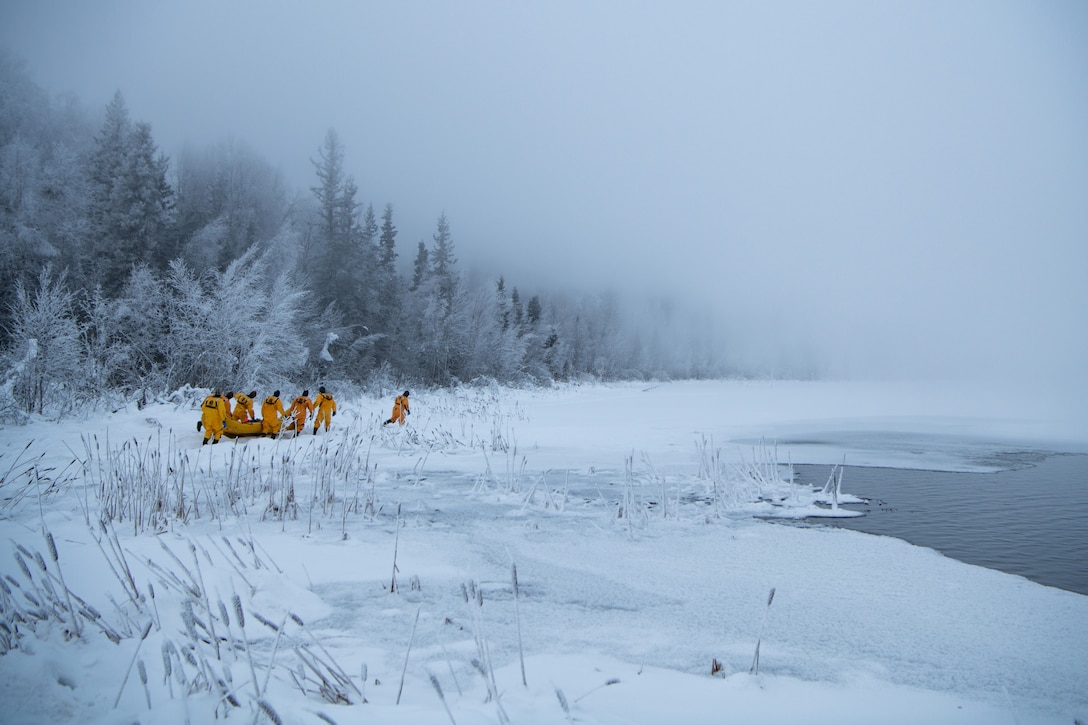 A group of airmen in yellow jackets pull a rubber raft toward an icy lake.