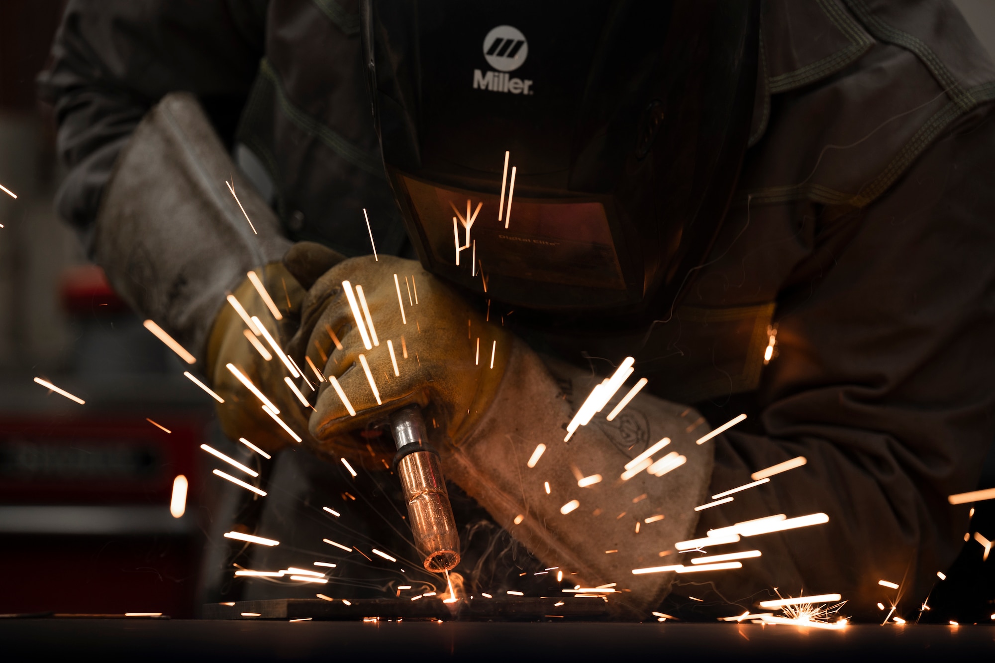 A welder uses a metallic inert gas welder to meld metal sheets together, causing orange sparks to fly.