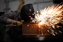 Sparks fly from a sheet of metal as a welder uses an oxygen acetylene torch.