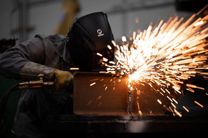Sparks fly from a sheet of metal as a welder uses an oxygen acetylene torch.
