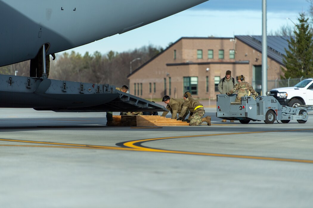 Photo of Airmen from the Vermont Air National Guard's 158th Aircraft Maintenance Squadron, along with Airmen from the New York ANG's 105th Airlift Wing, Stewart Air National Guard Base in Newburgh, New York, position wooden ramps to assist with loading equipment onto a C-17 Globemaster III aircraft at the Vermont Air National Guard Base, South Burlington, Vermont, Dec. 4, 2022.