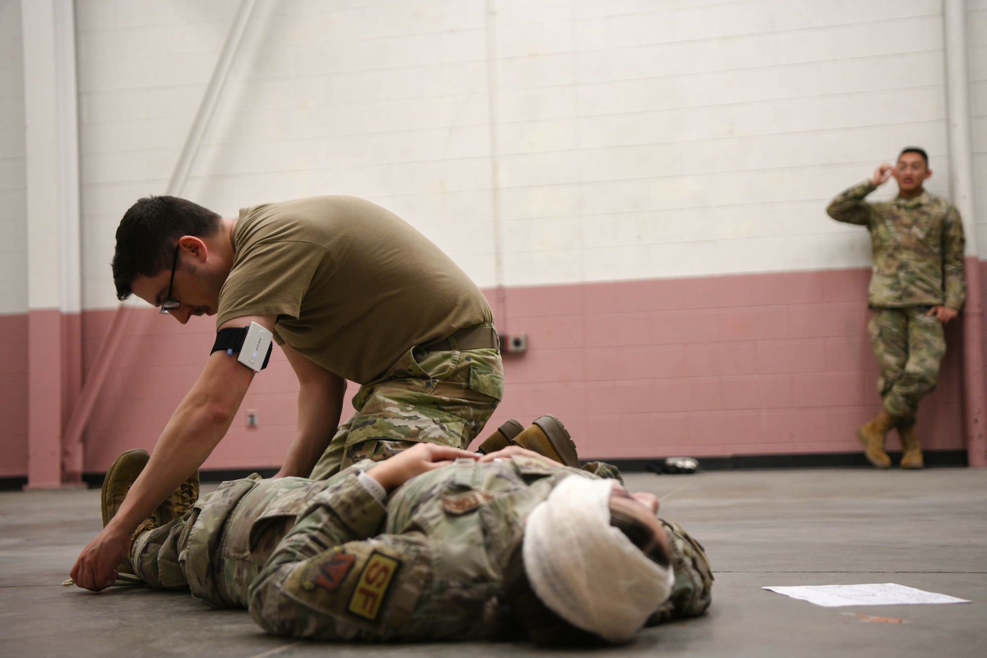 A man in a green shirt performs combat casualty care on a woman in a uniform.
