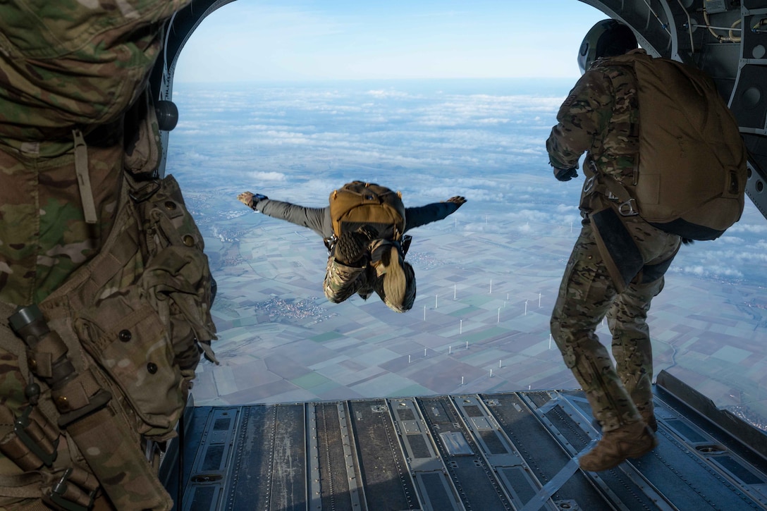 Service members jump out of a helicopter.
