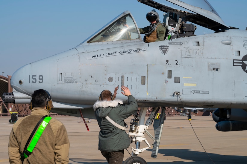 An airman directs a jet on a runway.